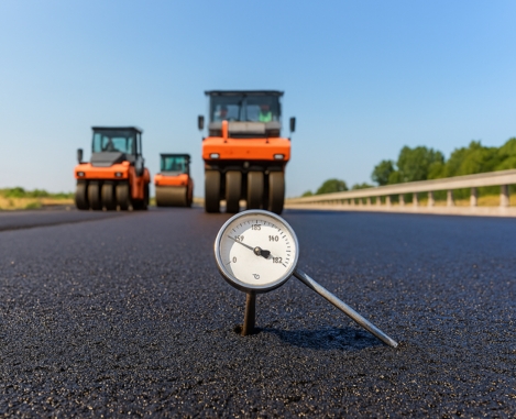 Temperature probe measuring fresh asphalt on a road, with rollers in the background